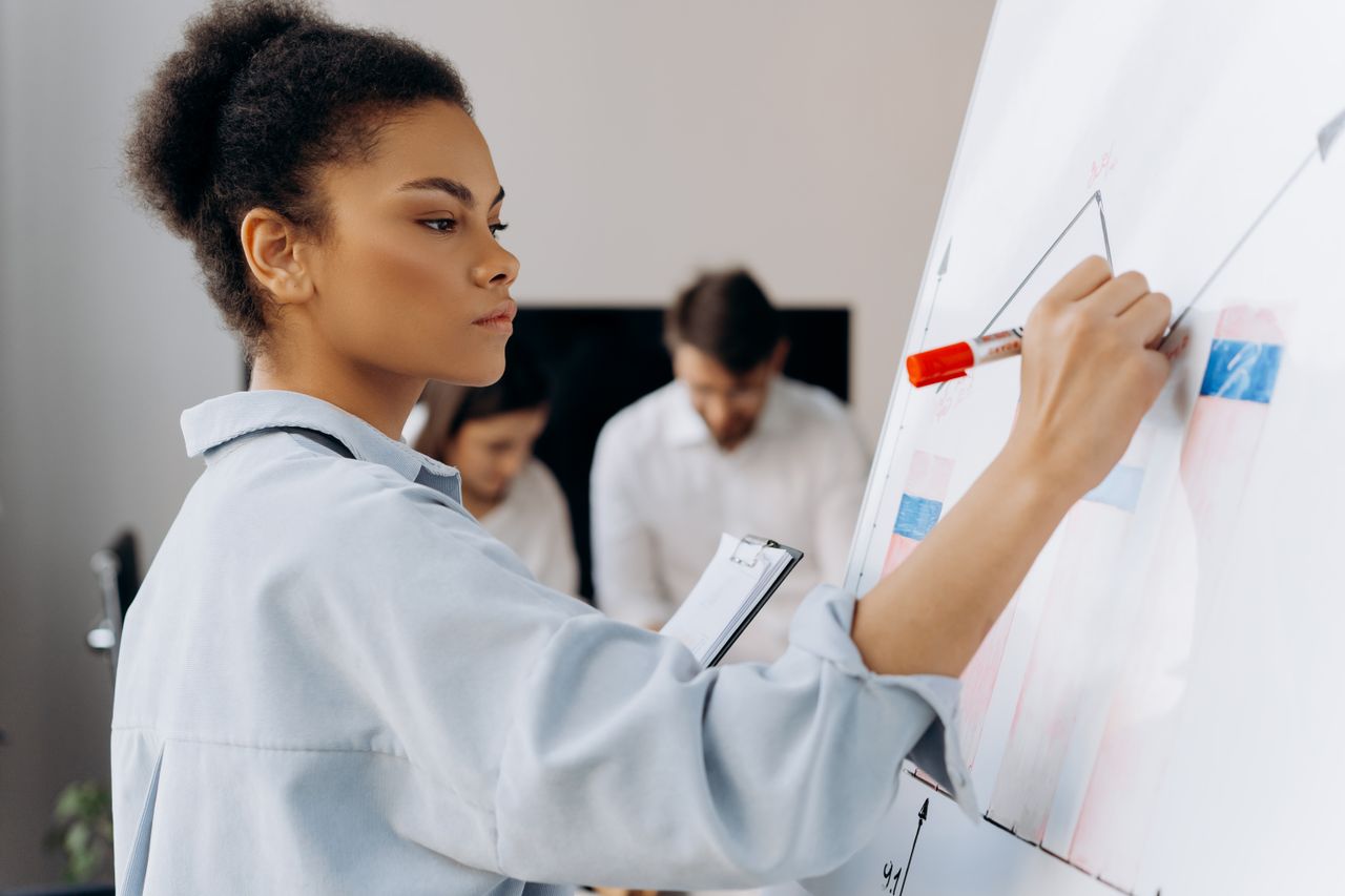 Crafting Captivating Headlines: Your awesome post title goes here Confident businesswoman illustrates data on whiteboard during a team meeting, showcasing collaborative analysis.